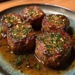 Beef tenderloin medallions served with garlic herb butter on a plate.