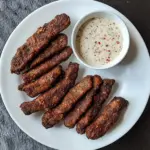 Fried venison cube steak fingers served with a dipping sauce on a plate.