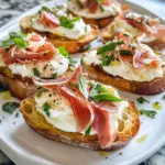 Burrata and prosciutto crostini garnished with fresh herbs on a wooden board