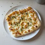 A plate of freshly made cottage cheese flatbread garnished with herbs.