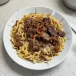 Delicious bowl of French onion beef and noodles with melted cheese and herbs