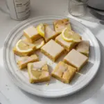 Fudgy lemon blondies on a white plate, drizzled with lemon glaze.