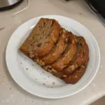 Slice of keto banana bread on a wooden table with bananas and nuts