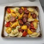 Sheet pan sausage and pierogies served with vegetables for a hearty meal.