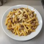 Creamy cheesy beef penne pasta dish topped with melted cheese and herbs