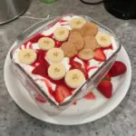 Delicious strawberry banana pudding dessert in a bowl, topped with fresh strawberries.