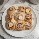 Freshly baked Cinnamon Banana Rolls drizzled with icing on a wooden table