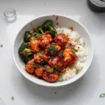 A plate of delicious Korean chicken garnished with sesame seeds and green onions.