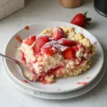 Strawberry Cheesecake Dump Cake topped with fresh strawberries and cream