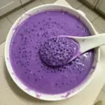 A bowl of purple yam sago dessert topped with coconut and colorful toppings.